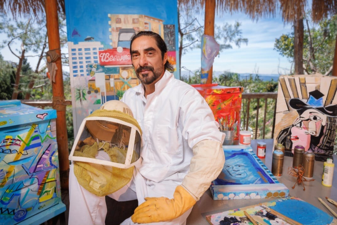 Steve in bee suit holding a colorful painted bee box at a partner sanctuary