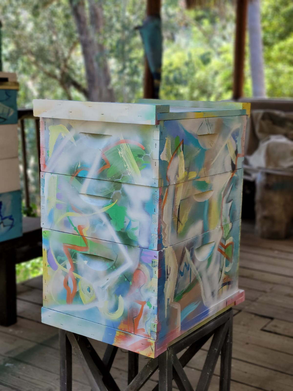 Beecasso painted bee box in soft white and pastel with fluid sprayed forms, on display stand