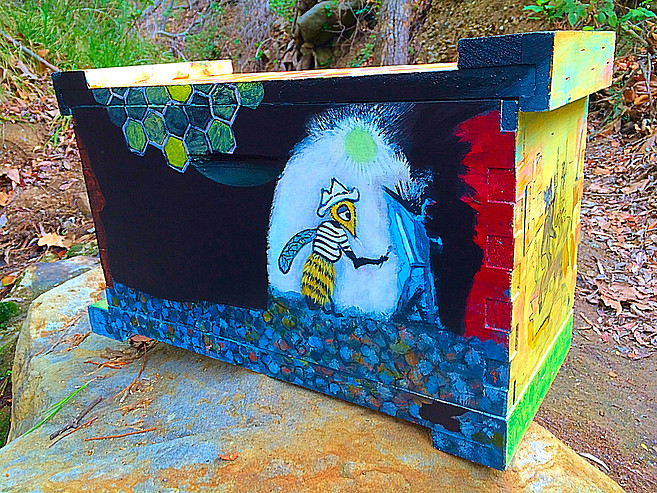 Beecasso painted bee box with Beecasso mascot character in white glowing circle on dark ground, honeycomb border