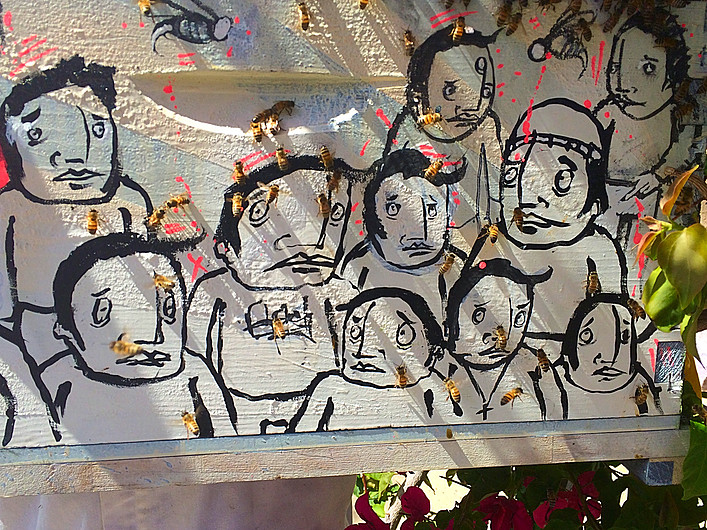 Beecasso bee box panel painted with grid of expressionist faces in black line on white, live bees walking on surface