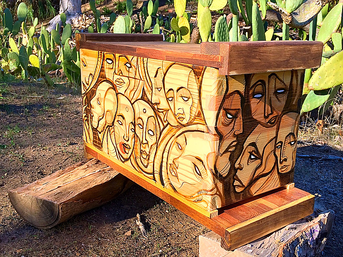 Beecasso wooden bee box with carved and painted overlapping face studies, warm wood tones