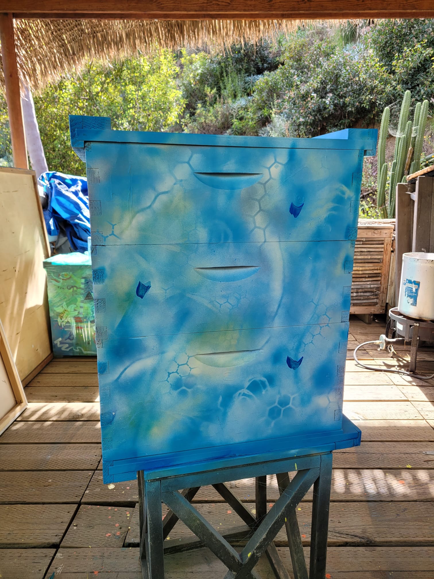 Beecasso painted bee box in sky blue with honeycomb stencil pattern, on display stand