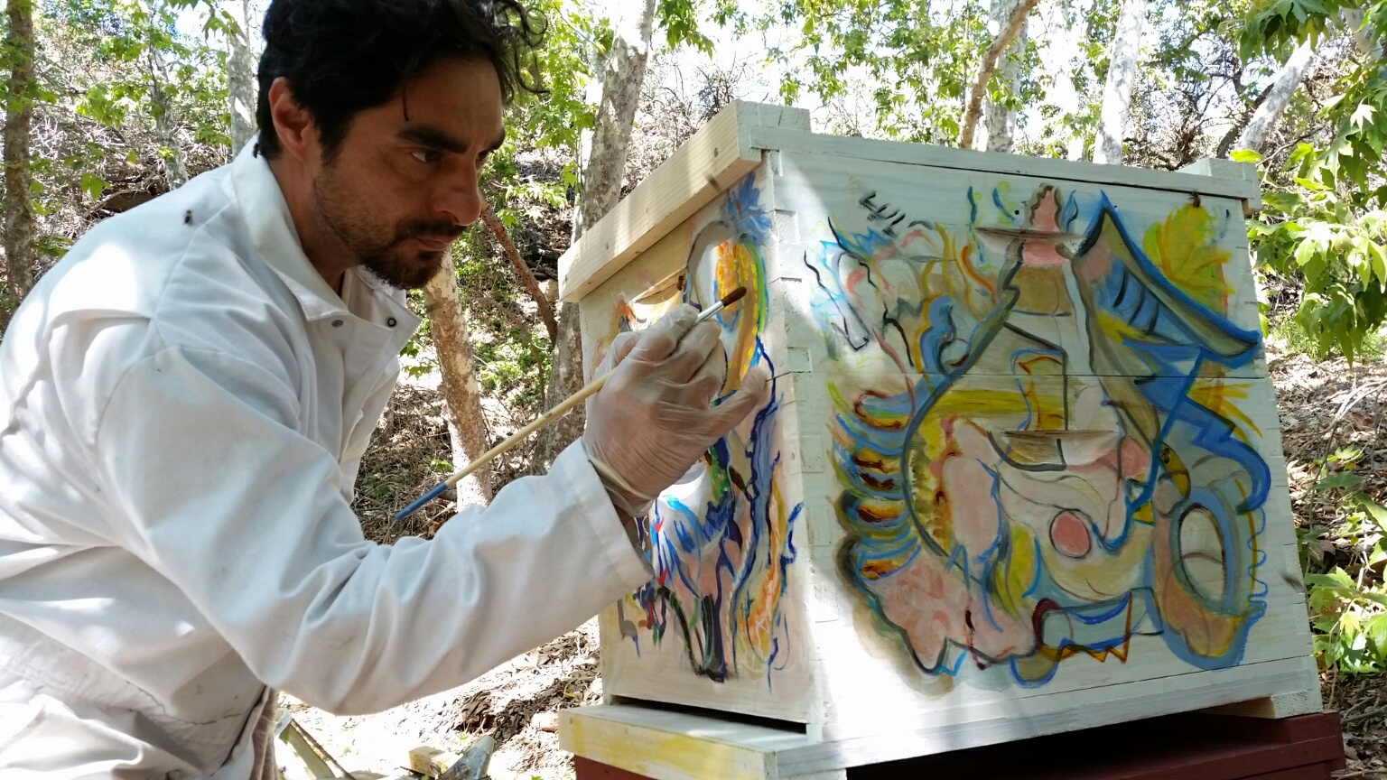 Steve Downs painting art on a bee box outdoors in the woods, in close detail