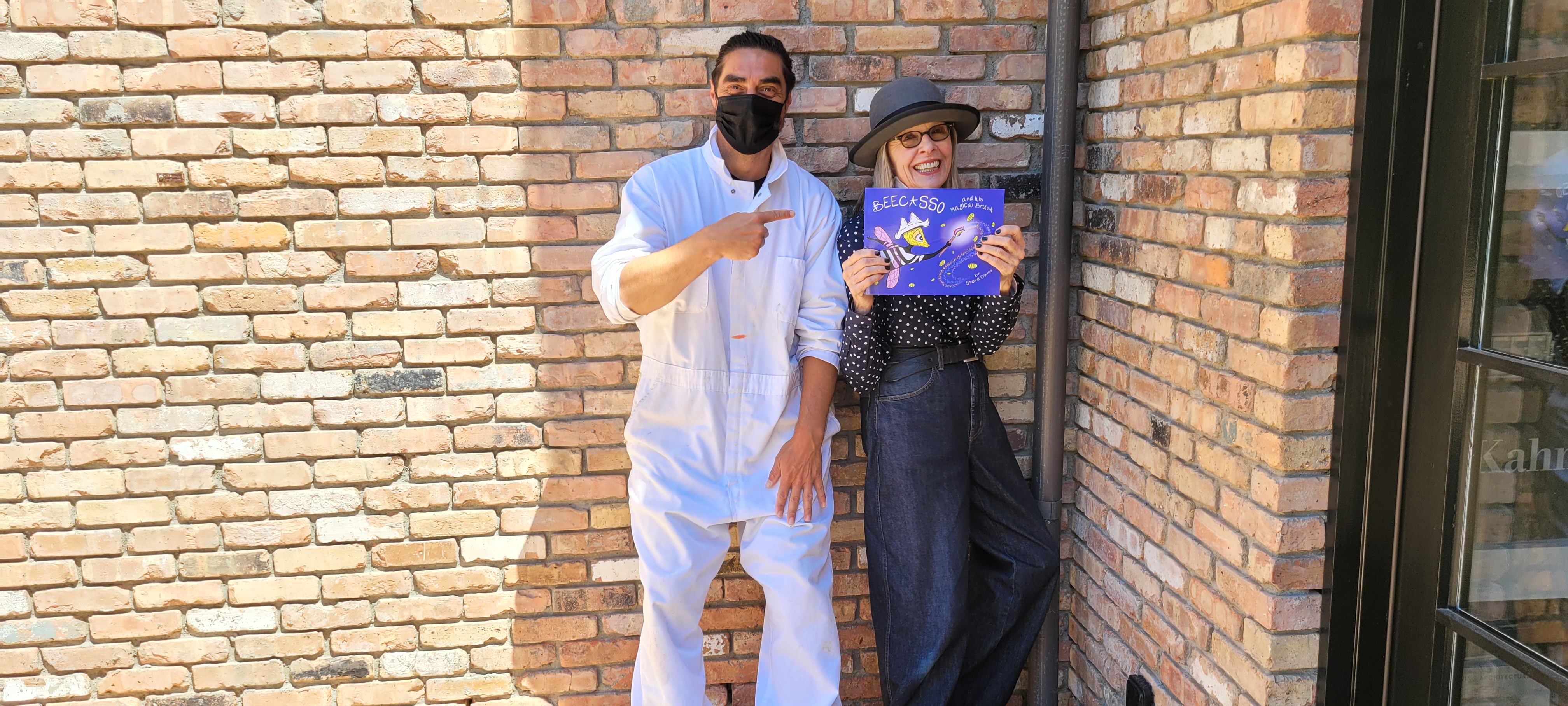Steve Downs in white work suit with unidentified woman holding a copy of Beecasso and His Magical Brush