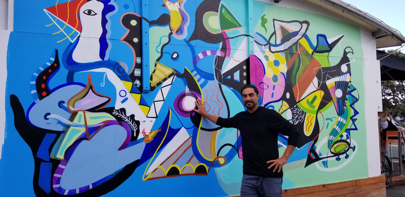 Steve Downs standing in front of his completed large outdoor cubist mural, arms spread