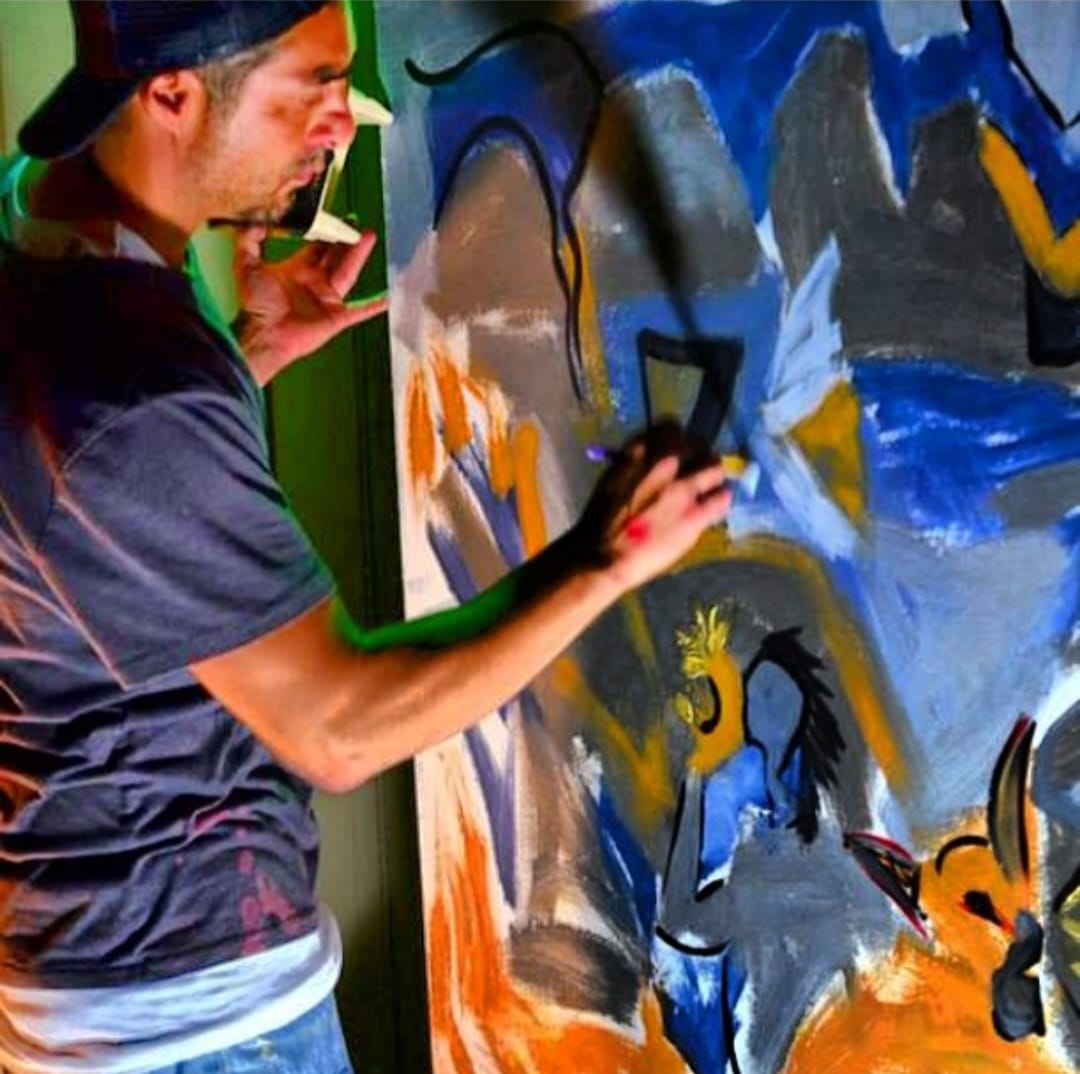 Steve Downs painting a large canvas indoors, blue and orange abstract forms taking shape