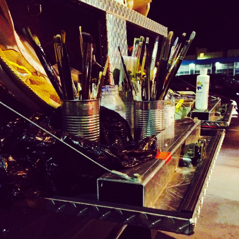 Steve Downs' artist toolkit, paint brushes in cans at a night painting event, city lights behind