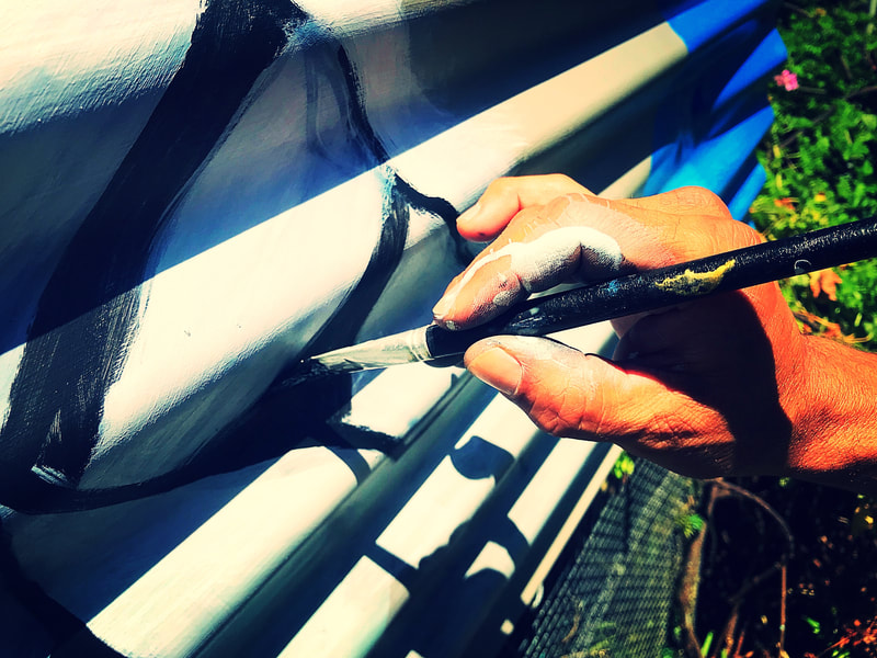Close-up of Steve Downs' hands painting precise black-and-white stripes on a bee box surface