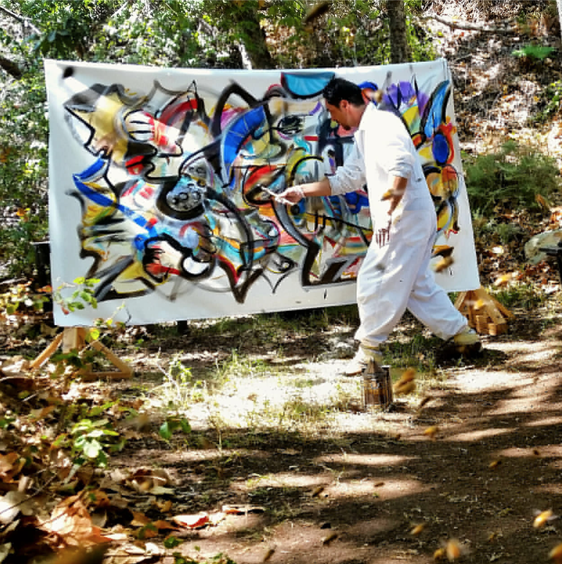 Steve Downs in white suit holding a large abstract canvas outdoors in a wooded setting