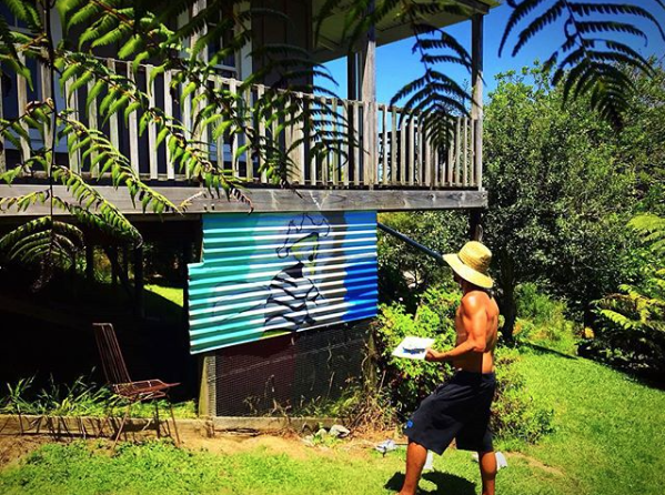 Steve Downs in garden setting with tropical plants and a painted canvas or mural visible