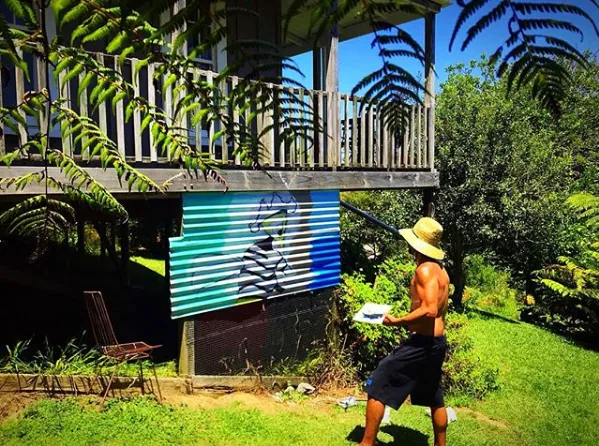 Steve Downs in garden setting with tropical plants and a painted canvas or mural visible