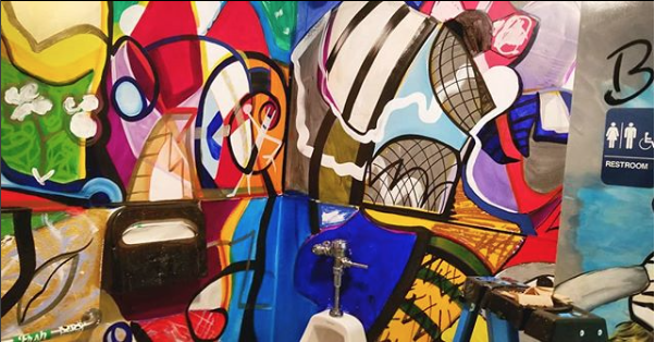 Beecasso mural painted on exterior public bathroom wall, colorful figurative and abstract forms