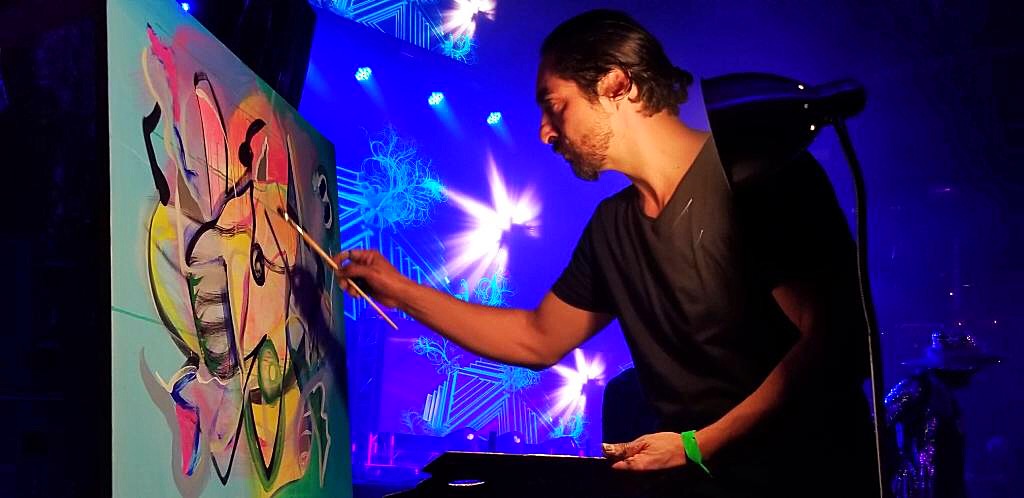 Steve Downs painting live on stage at a concert event under blue stage lighting