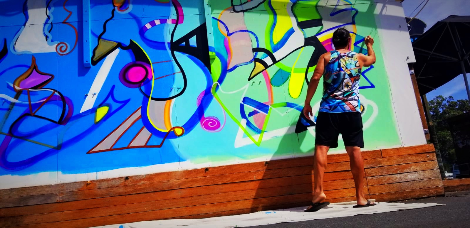Steve Downs painting the New Zealand outdoor mural, colorful abstract forms on large exterior wall