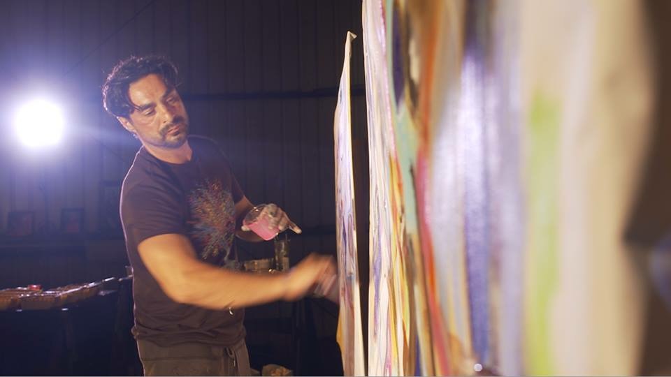 Steve Downs painting large vertical canvases under stage lighting at a Beecasso art show