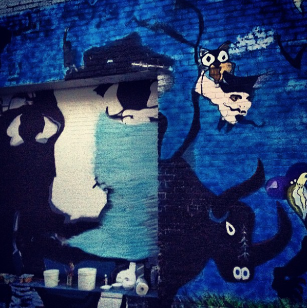 Outdoor wall mural by Steve Downs, dark shadowy figure with bee character on brick