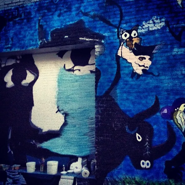 Outdoor wall mural by Steve Downs, dark shadowy figure with bee character on brick